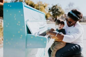an adult child play a colourful piano outdoors