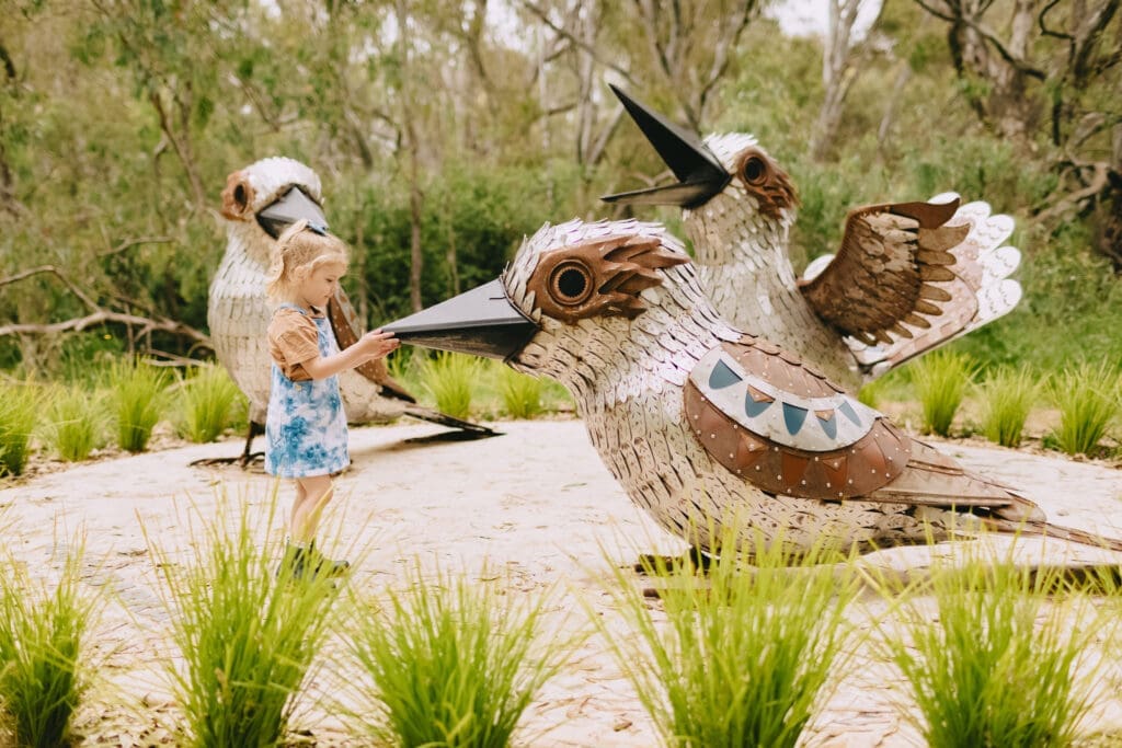 A child stands amongst three large sculptures of laughing kookaburras.