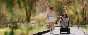 A woman in a wheelchair with a dog on her lap and another woman walk along the boardwalk at the Murray River, Albury