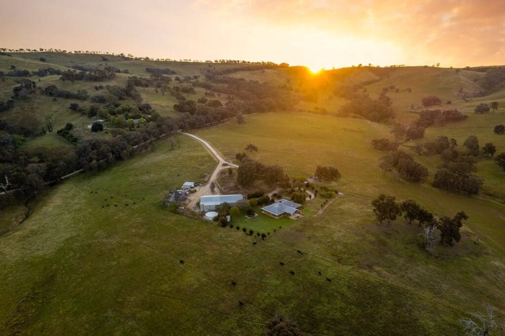 Aerial view of Huon Creek Retreat accommodation surrounded by farmland, rolling hills and a sunset