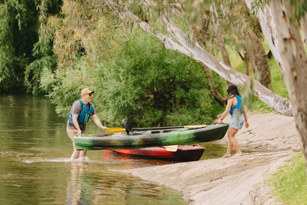 A couple pull canoes out of the water on the banks of the Murray River